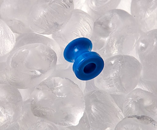 Photo of a micro ear drain tube for ENT medical devices, shown on clear resin pellets, by Isometric Micro Molding