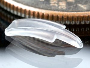 Image of micro ophthalmic ocular implant glaucoma drain for medical devices, shown next to a coin, by Isometric Micro Molding