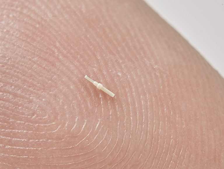 Photo of a micro pin assembly for micro electronics and communications, shown on a finger tip, by Isometric Micro Molding