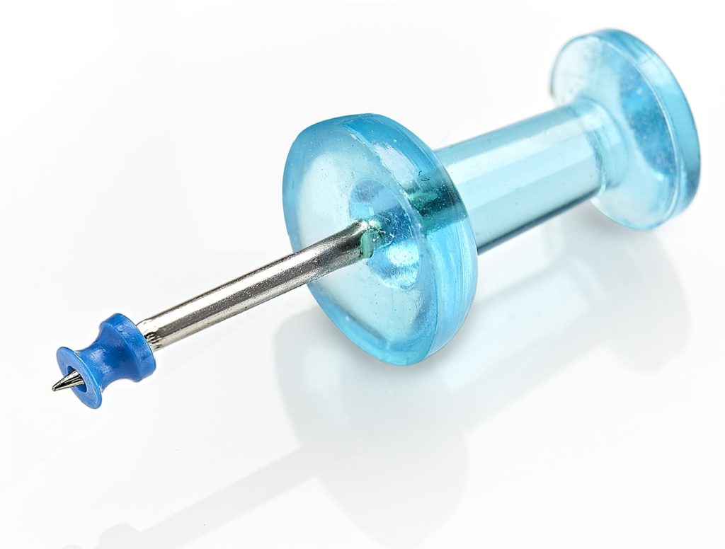 Photo of micro ear drain tube for ENT medical devices, with thin wall molding, shown on the tip of a thumbtack, by Isometric Micro Molding