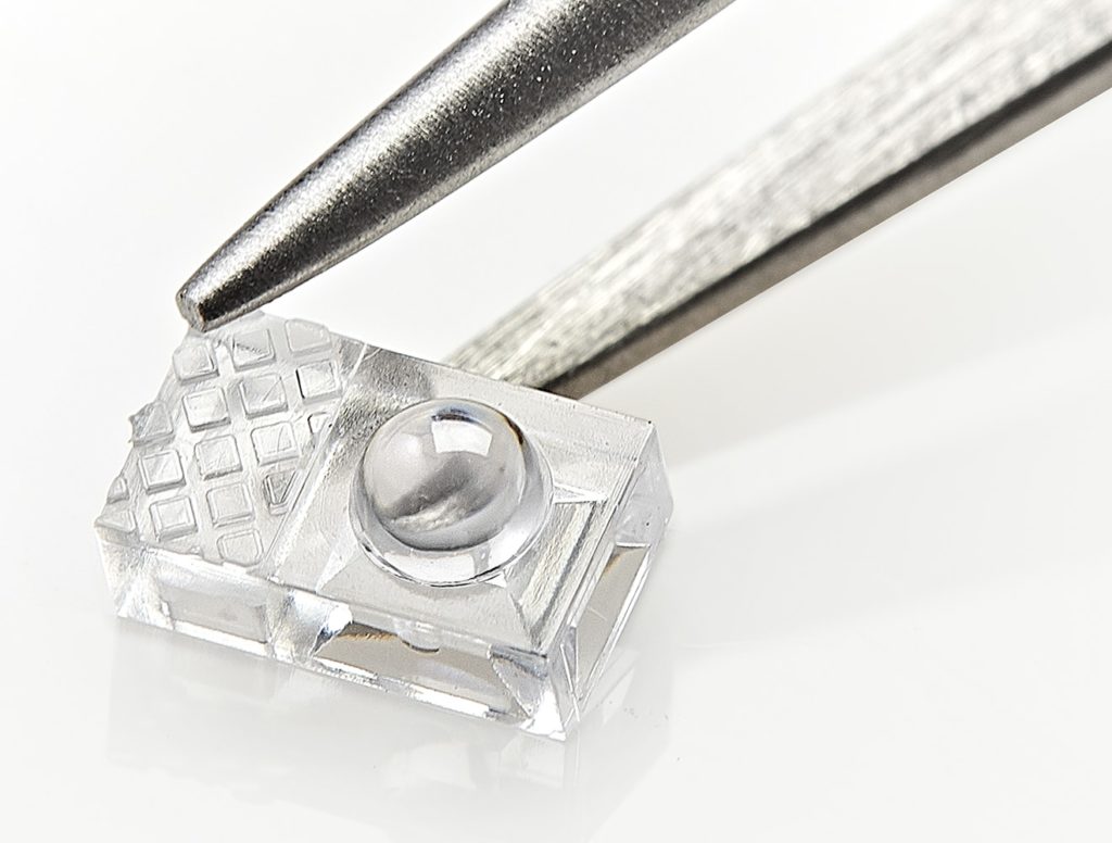 Photo of miicro optics lens for medical devices, shown on the tip of a tweezer, by Isometric Micro Molding.