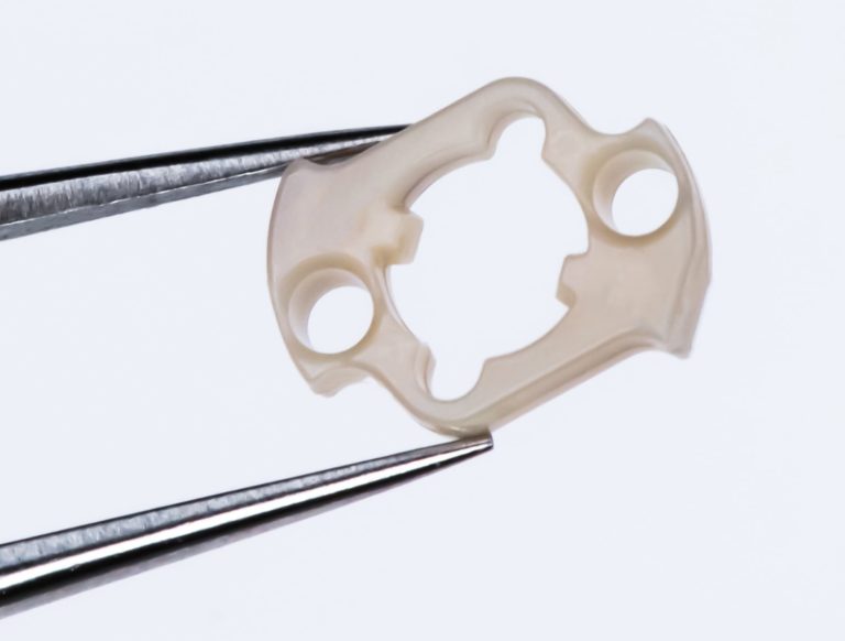 Photo of PEEK surgical tool micro component for robotic surgery medical devices, shown on the tip of a tweezer, by Isometric Micro Molding