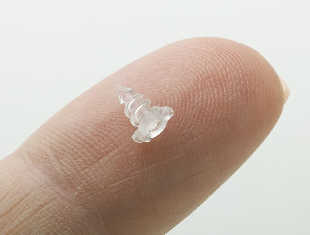 Photo of a bioresorbable micro tissue repair screw for orthopedic medical devices, shown on a finger tip, by Isometric Micro Molding
