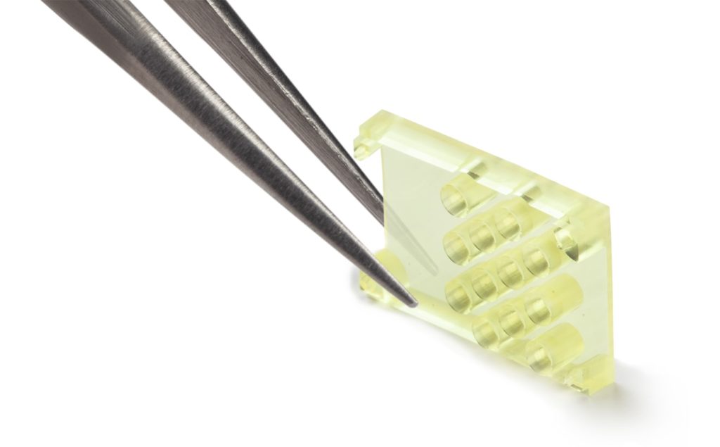 Photo of lens micro component for medical devices and micro electronics, shown on the tip of a tweezer, by Isometric Micro Molding