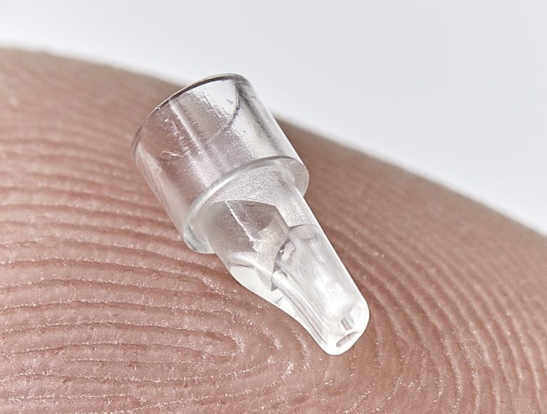 Photo of drug dispensing micro part for drug delivery medical devices, shown on a fingertip, made with medical grade class IV PET, by Isometric Micro Molding